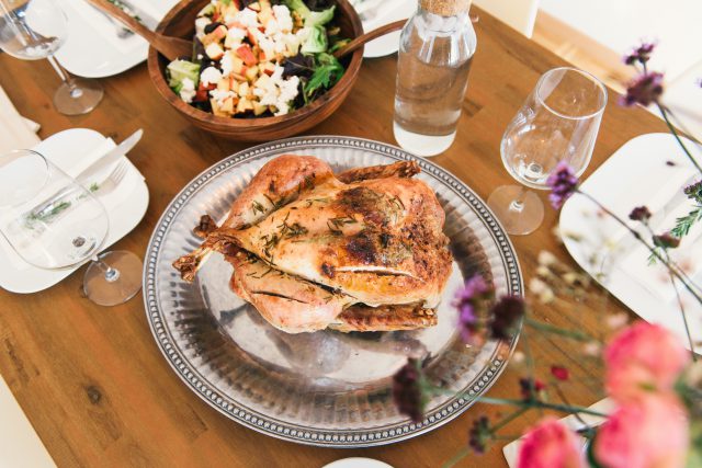 Thanksgiving: turkey on a silver platter with glasses and salad around it on a wooden table